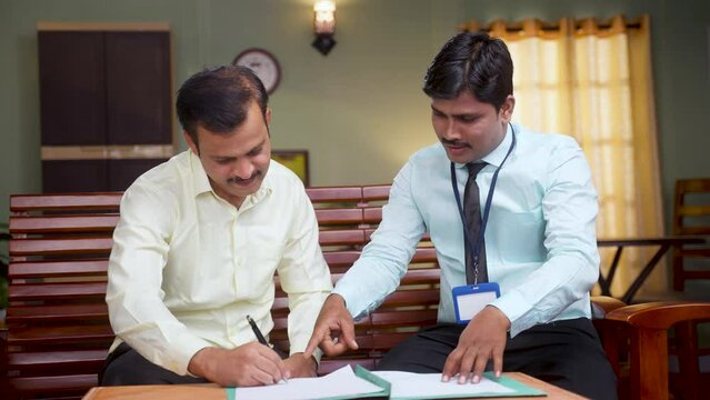 Banking officer taking sign on insurance documents from middle aged man at home - concept of financial, investment and loan agreement or deal.