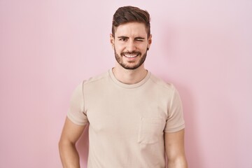 Hispanic man with beard standing over pink background winking looking at the camera with sexy expression, cheerful and happy face.