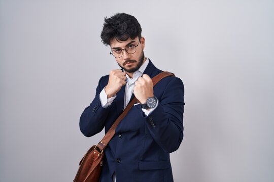 Hispanic man with beard wearing business clothes ready to fight with fist defense gesture, angry and upset face, afraid of problem