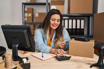 Young beautiful plus size woman ecommerce business worker counting dollars using calculator at...