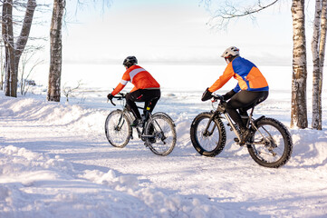 Two men in bright sportswear ride sports bikes in the park in winter