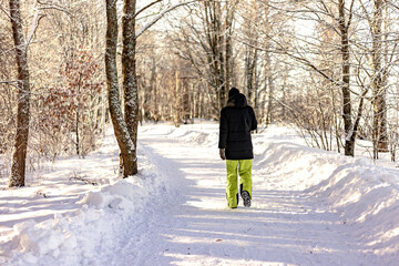 Fototapeta na wymiar A man in a dark jacket and yellow sweatpants walks in a winter park