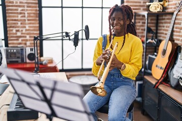 African american woman musician smiling confident holding trumpet at music studio