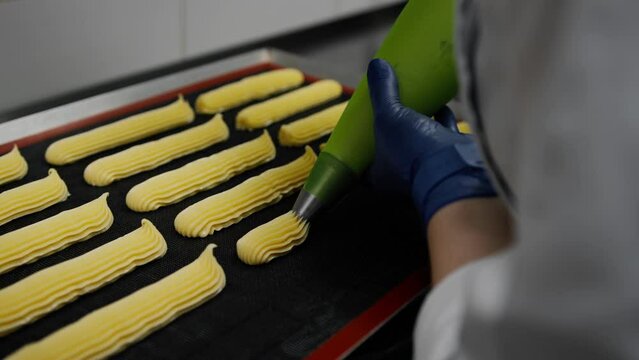 The kitchen in the bakery - the process of preparing an eclair a woman baker applies a delicious cream on a baking sheet