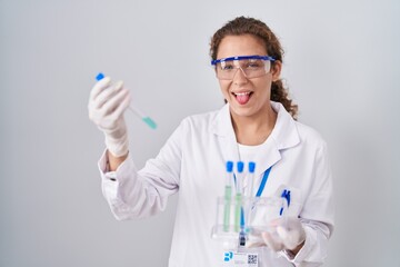 Young caucasian scientist woman working with laboratory samples sticking tongue out happy with...