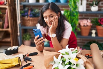 Young beautiful hispanic woman florist smiling confident using smartphone at flower shop
