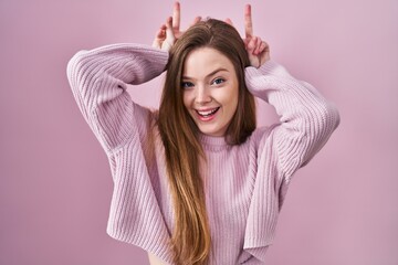 Young caucasian woman standing over pink background posing funny and crazy with fingers on head as...