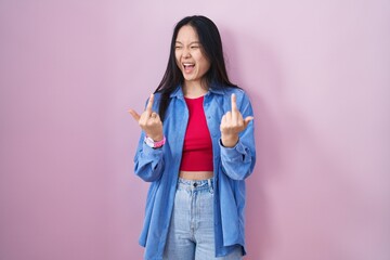 Young asian woman standing over pink background showing middle finger doing fuck you bad...