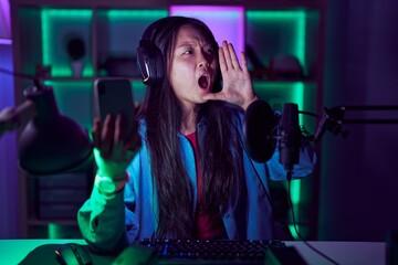 Young asian woman playing video games with smartphone shouting and screaming loud to side with hand on mouth. communication concept.