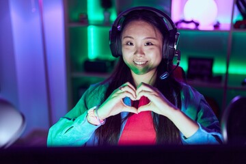 Young chinese woman streamer smiling confident doing heart symbol with hands at gaming room