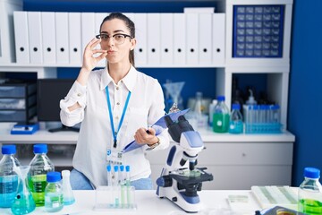 Young brunette woman working at scientist laboratory mouth and lips shut as zip with fingers....