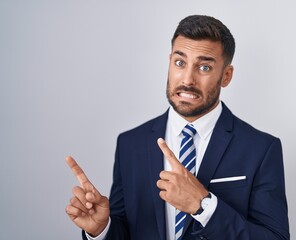 Handsome hispanic man wearing suit and tie pointing aside worried and nervous with both hands, concerned and surprised expression