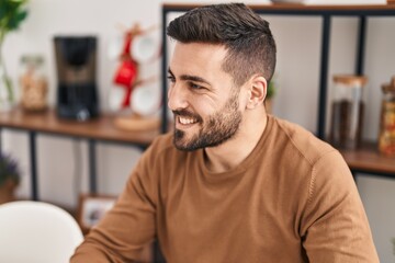 Young hispanic man smiling confident sitting on table at home