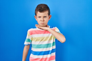 Young caucasian kid standing over blue background cutting throat with hand as knife, threaten aggression with furious violence