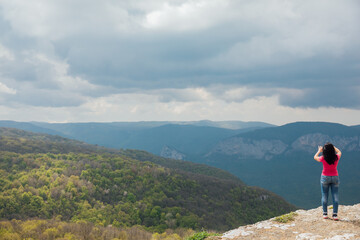 Naklejka na ściany i meble a woman stands on a mountain and photographs nature hiking journey