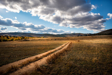 dirt road going into the distance under a sky with dark clouds in autumn
