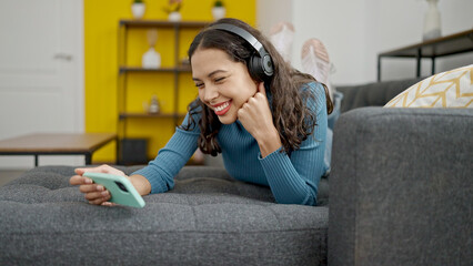 Fototapeta premium Young beautiful hispanic woman watching video on smartphone lying on the sofa at home