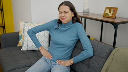 Young beautiful hispanic woman suffering for menstrual pain sitting on the sofa at home