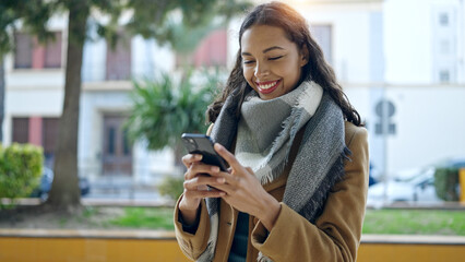 Young beautiful hispanic woman using smartphone smiling at park