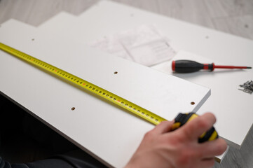 Furniture assembler measures a wooden board with a tape measure, close-up. Construction concept, handyman,furniture assembly