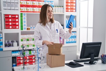 Young woman pharmacist using touchpad unboxing package at pharmacy