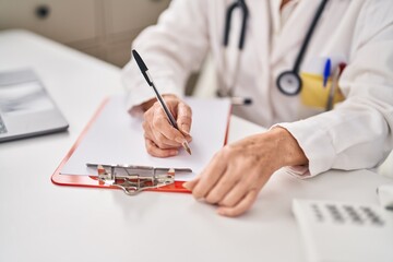 Fototapeta premium Middle age woman wearing doctor uniform writing on paperwork at clinic