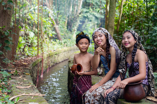 Asian two girls in beautiful batik suit and boy sitting by the river. One girl points towards the camera