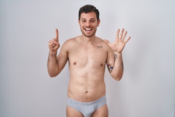 Fototapeta premium Young hispanic man standing shirtless wearing underware showing and pointing up with fingers number six while smiling confident and happy.