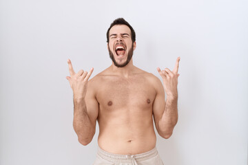 Fototapeta premium Young hispanic man standing shirtless over white background shouting with crazy expression doing rock symbol with hands up. music star. heavy concept.