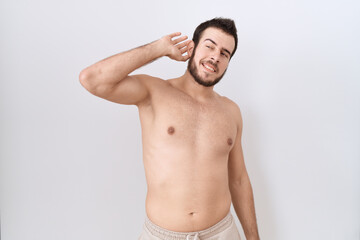 Young hispanic man standing shirtless over white background smiling with hand over ear listening an hearing to rumor or gossip. deafness concept.