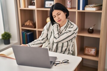 Young chinese woman studying sitting on table suffering for backache at home