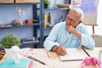 Senior grey-haired man artist drawing on notebook with doubt expression at art studio