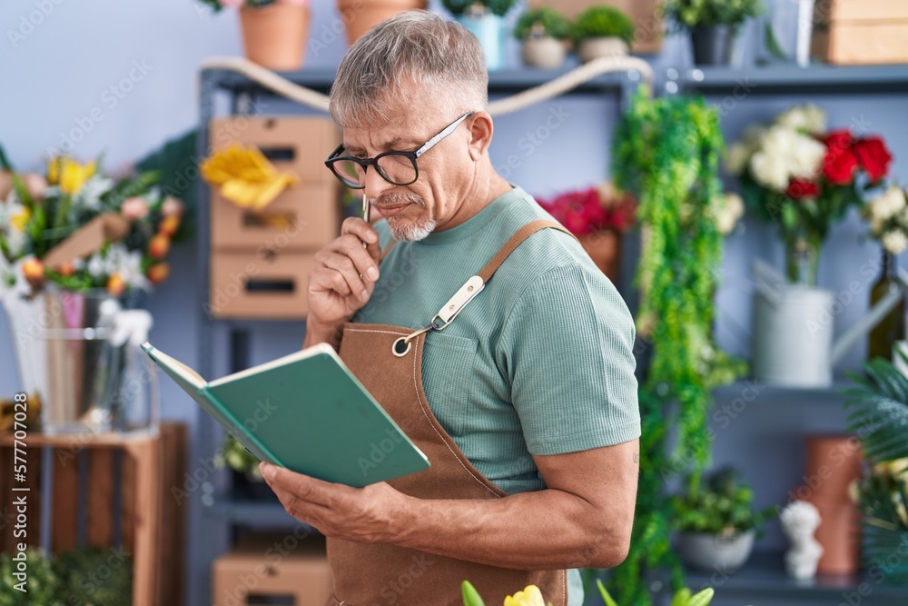 Poster middle age grey-haired man florist reading book at flower shop