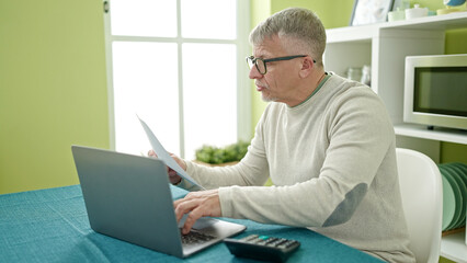 Middle age grey-haired man using laptop reading document at home