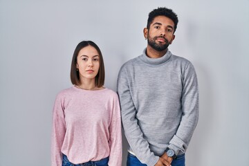 Young hispanic couple standing together relaxed with serious expression on face. simple and natural looking at the camera.