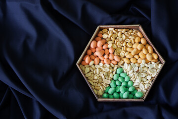 Six varieties of multi-colored roasted glazed peanuts in a hexagonal craft box against a dark blue...