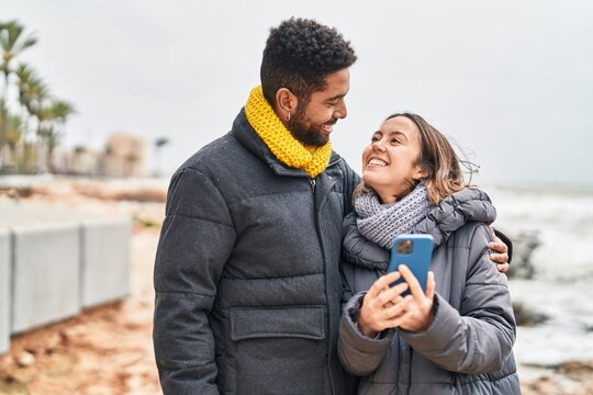 Man and woman couple smiling confident using smartphone at seaside