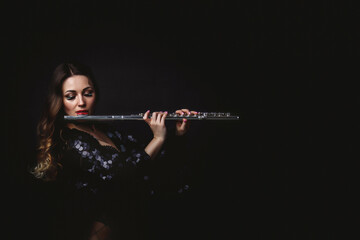 Pretty cover artist woman playing on flute at black isolated background, closed eyes. Chic lady...