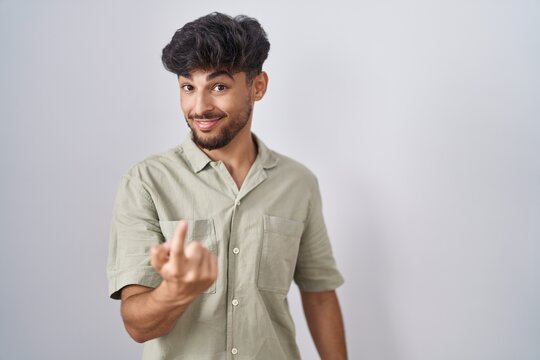 Arab man with beard standing over white background beckoning come here gesture with hand inviting welcoming happy and smiling