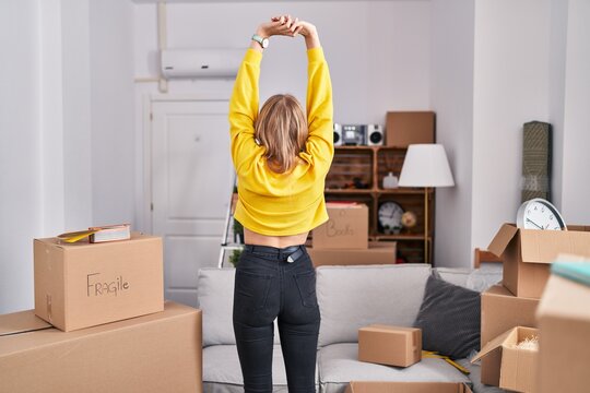 Young blonde woman stretching arms standing on back view at new home