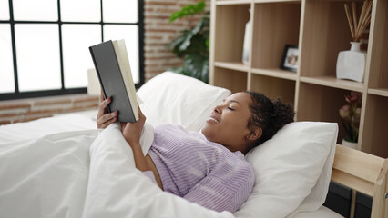African american woman reading book lying on bed at bedroom