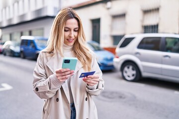 Young blonde woman using smartphone and credit card at street
