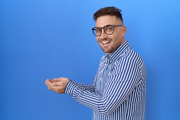 Fototapeta premium Hispanic man with beard wearing glasses pointing aside with hands open palms showing copy space, presenting advertisement smiling excited happy