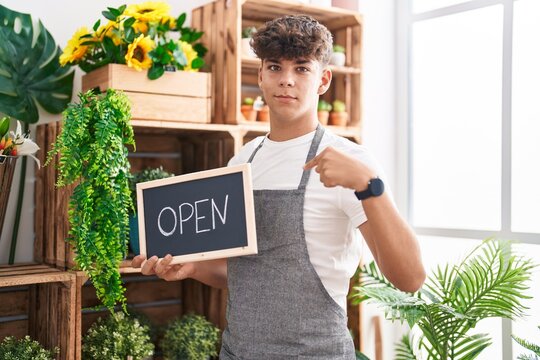 Hispanic teenager working at florist holding open sign pointing finger to one self smiling happy and proud