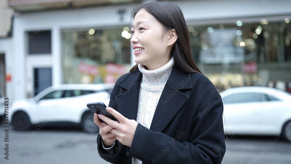 Wall mural Young chinese woman smiling confident using smartphone at street