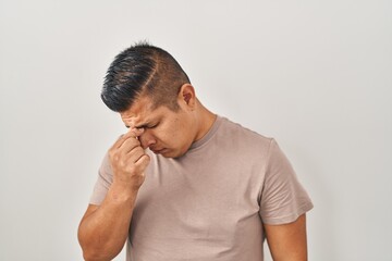 Hispanic young man standing over white background tired rubbing nose and eyes feeling fatigue and headache. stress and frustration concept.