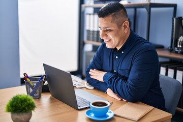Young latin man business worker smiling confident sitting on table at office