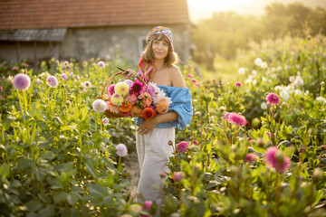 Portrait of a young stylish woman stands with a basket full of colorful freshly picked up dahlias...