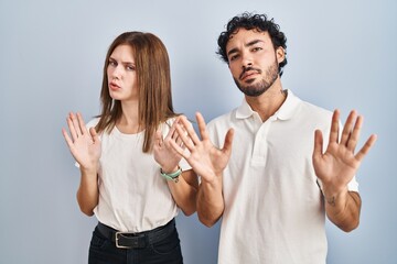 Young couple wearing casual clothes standing together moving away hands palms showing refusal and denial with afraid and disgusting expression. stop and forbidden.