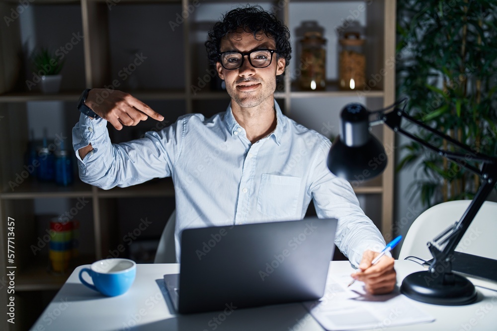 Poster Hispanic man working at the office at night looking confident with smile on face, pointing oneself with fingers proud and happy.